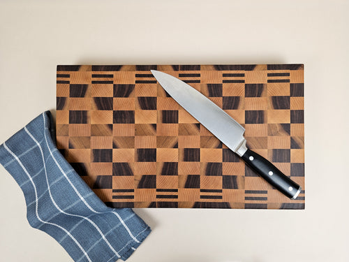 Wooden checkerboard cutting board with a knife and a blue tea towel on a beige background